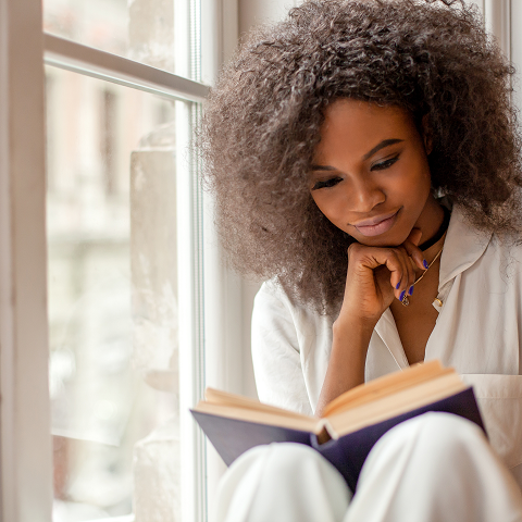 Pretty afro-american girl with reading a book sitting on the windowsill.