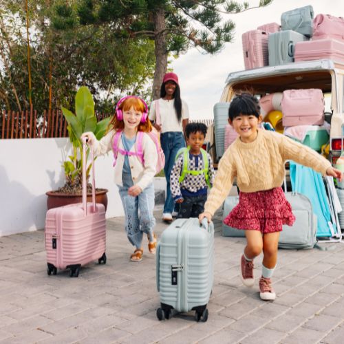 Group of children sitting on an orange couch with kids travel suitcases and bags in front of them