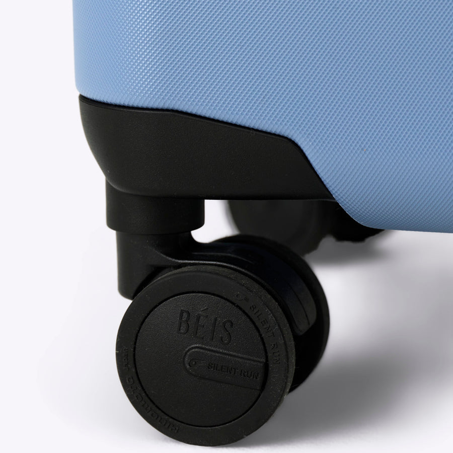 Close-up of a light blue suitcase with 'Béis' branding on a white background