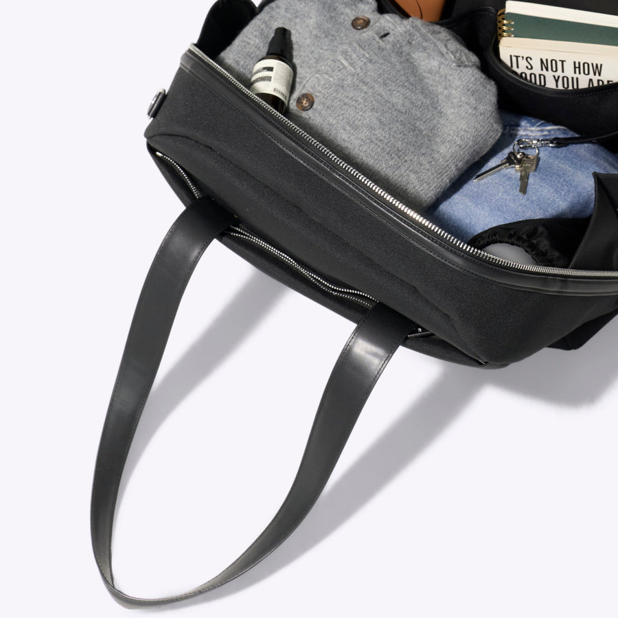 Black backpack with items including a book and a plush toy on a white background