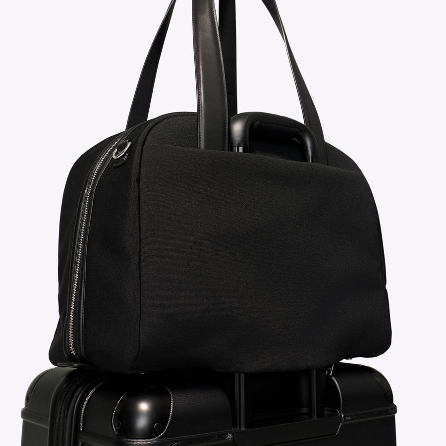 Black duffel bag on top of a black suitcase against a white background