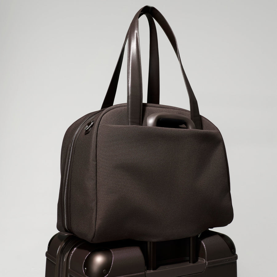 Black handbag stacked on top of a black suitcase against a light gray background