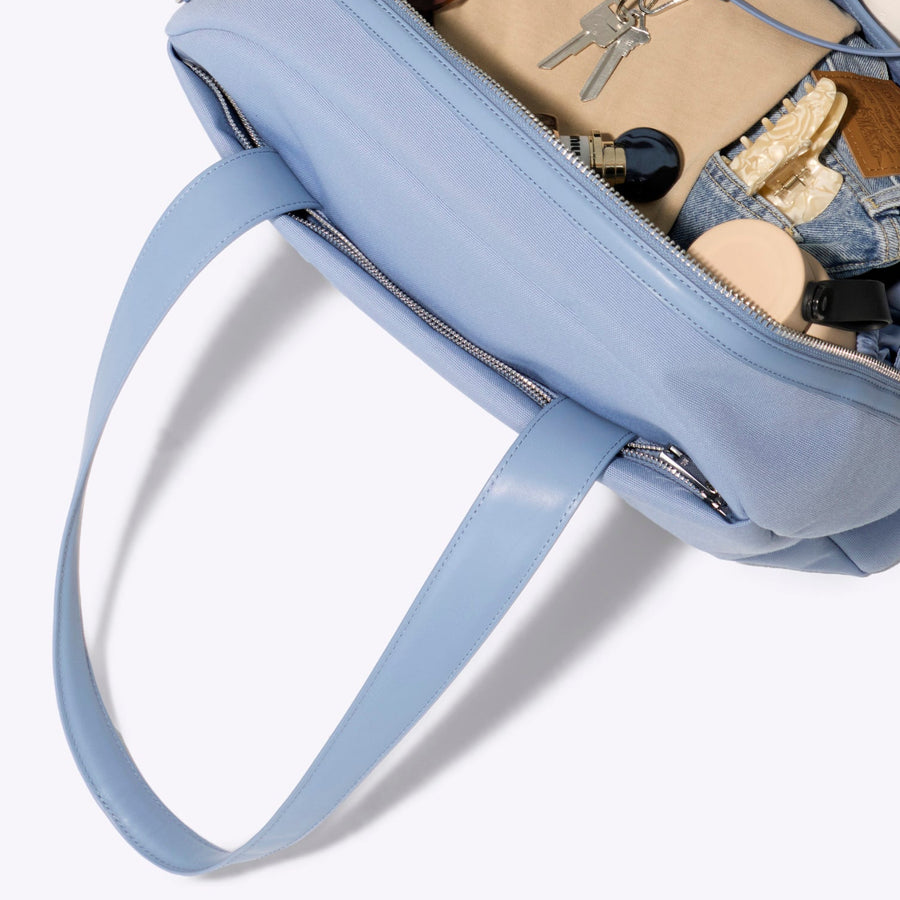 Light blue backpack with sunglasses and other items on a white background