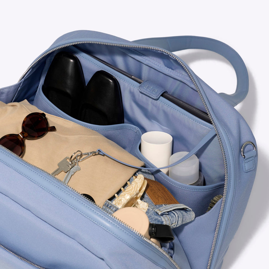 Light blue backpack with compartments containing sunglasses, a book, and a water bottle on a white background