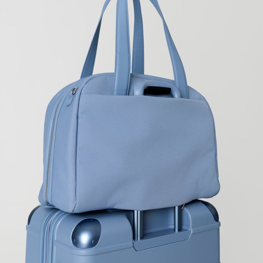 Light blue duffel bag on top of a matching suitcase against a light gray background