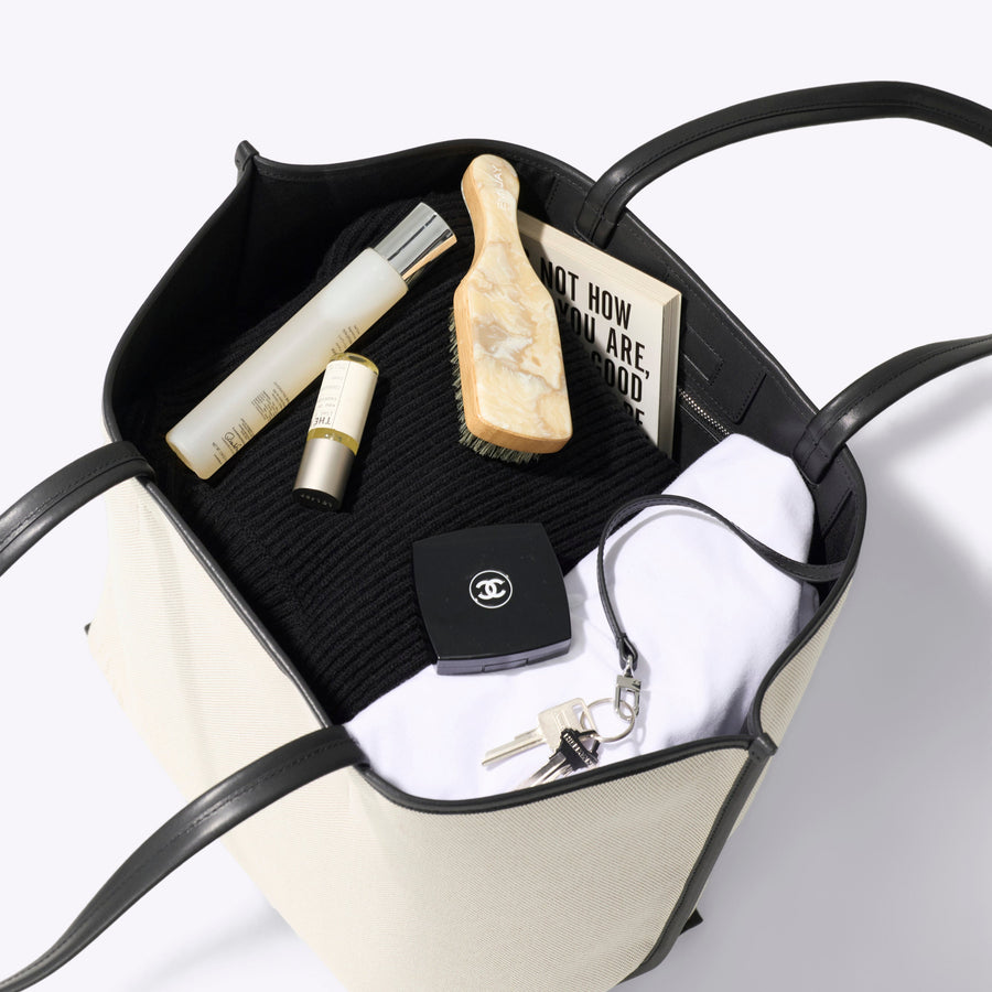 Black and beige handbag with personal items on a white background