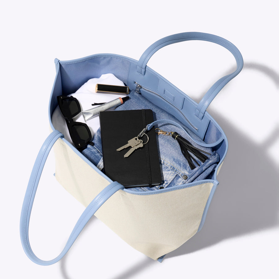 Blue and beige handbag with items inside on a white background