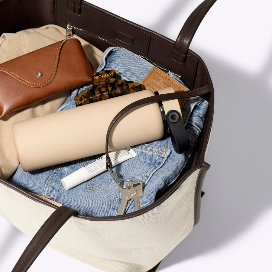 Tote bag with compartments containing a brown wallet, rolled-up paper, and denim item on a light gray background