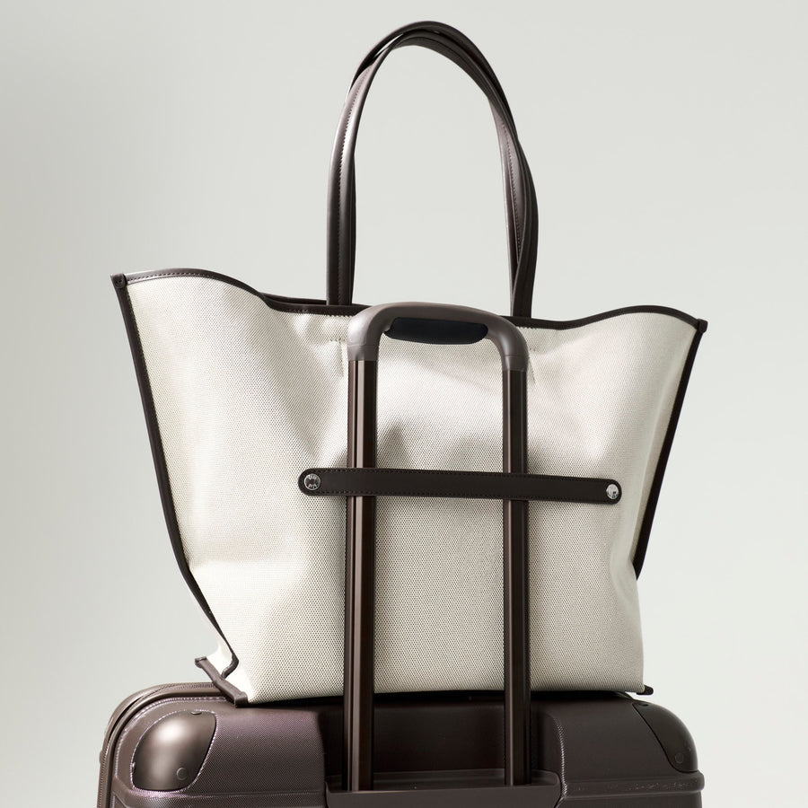 White tote bag with black handles on a dark suitcase against a light gray background